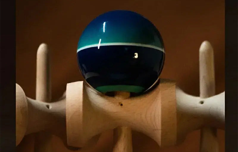 Close-up of a Tasse wooden kendama with a glossy teal and dark blue ball, white stripe detail, and warm brown background.