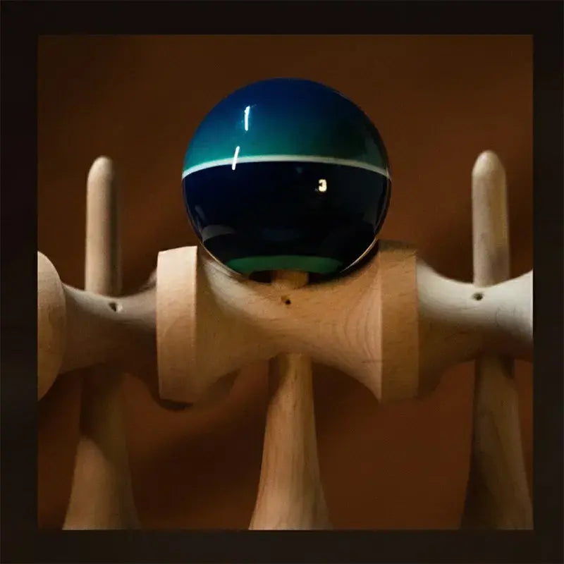 Close-up of a Tasse wooden kendama with a glossy teal and dark blue ball, white stripe detail, and warm brown background.