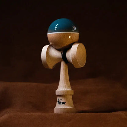 Tasse wooden kendama with a glossy blue and natural wood ball, white stripe detail, and natural wood handle, displayed upright on a warm brown background.