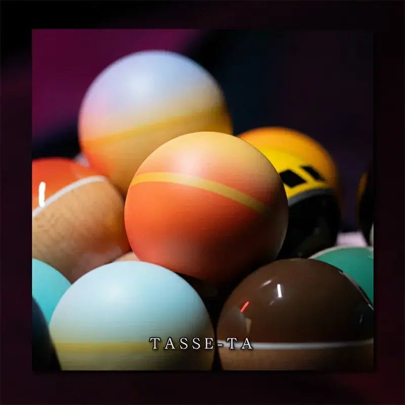 Close-up of multiple kendama balls in assorted colors and finishes, featuring an orange gradient ball in the center against a dark background.