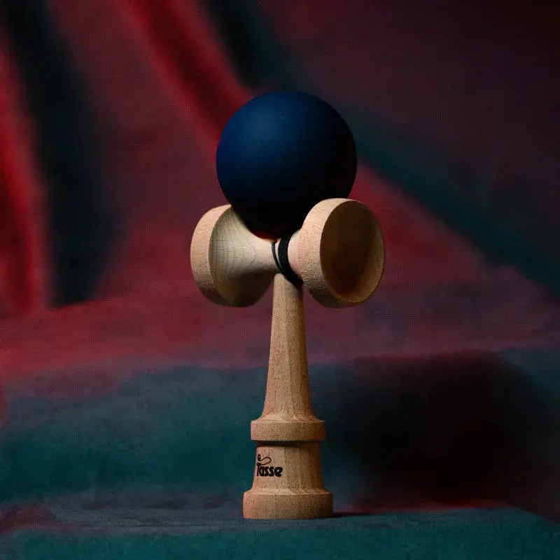 Tasse wooden kendama with a matte dark blue ball and natural wood handle, displayed upright on a red and blue gradient background.