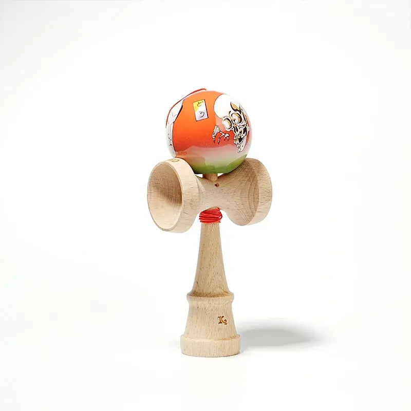 HUN kendama with an illustrated orange-green ball, skull artwork, red string, and natural wood handle, isolated on a light background.