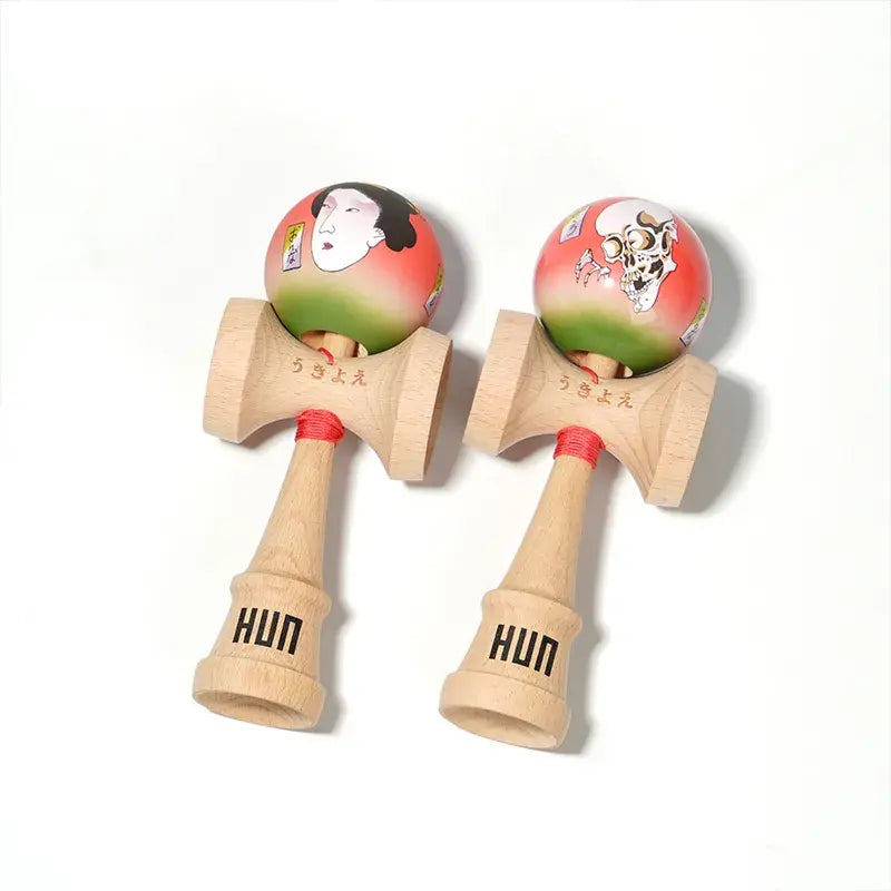 Two HUN kendamas with illustrated red-green balls, featuring Japanese-style portrait and skull artwork, displayed side by side on a light background.
