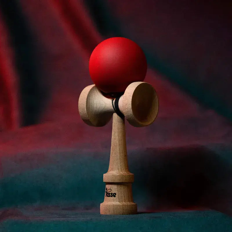 Tasse wooden kendama with a matte red ball and natural wood handle, displayed upright on a red and blue gradient background.