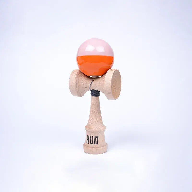 HUN Kendama Kylin Model with a glossy light pink and bright orange ball, natural wood handle, and light background.