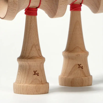 Close-up of two HUN kendama natural wood handles featuring red string wraps and K2 engraving details on a light background.