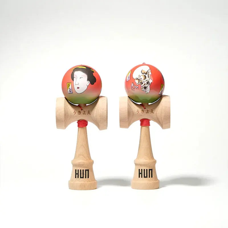 Two HUN kendamas with illustrated red-green balls, featuring Japanese-style portrait and skull artwork, displayed side by side on a light background.