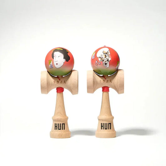 Two HUN kendamas with illustrated red-green balls, featuring Japanese-style portrait and skull artwork, displayed side by side on a light background.