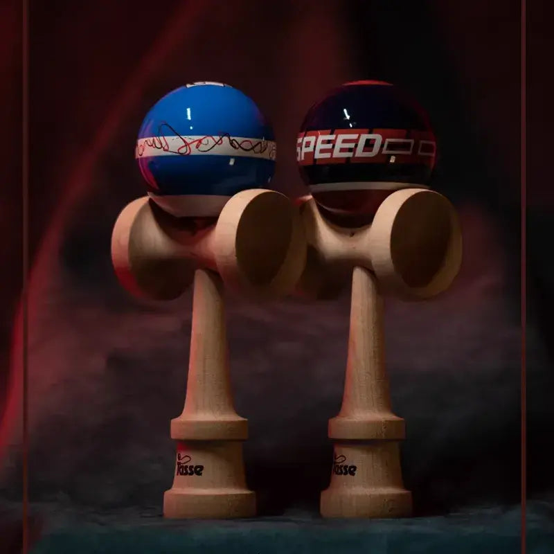 Two Tasse wooden kendamas with graphic blue and navy balls, including line art detail and “SPEED” text, displayed side by side on a dark red and blue background.