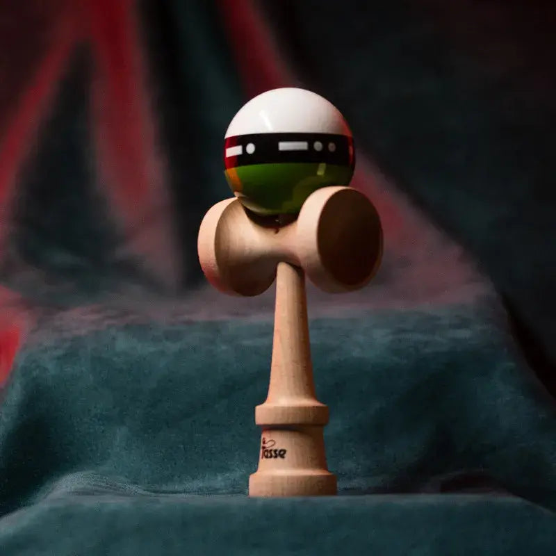 Tasse wooden kendama with a glossy white and green ball, black graphic band detail, and natural wood handle, displayed upright on a red and blue background.
