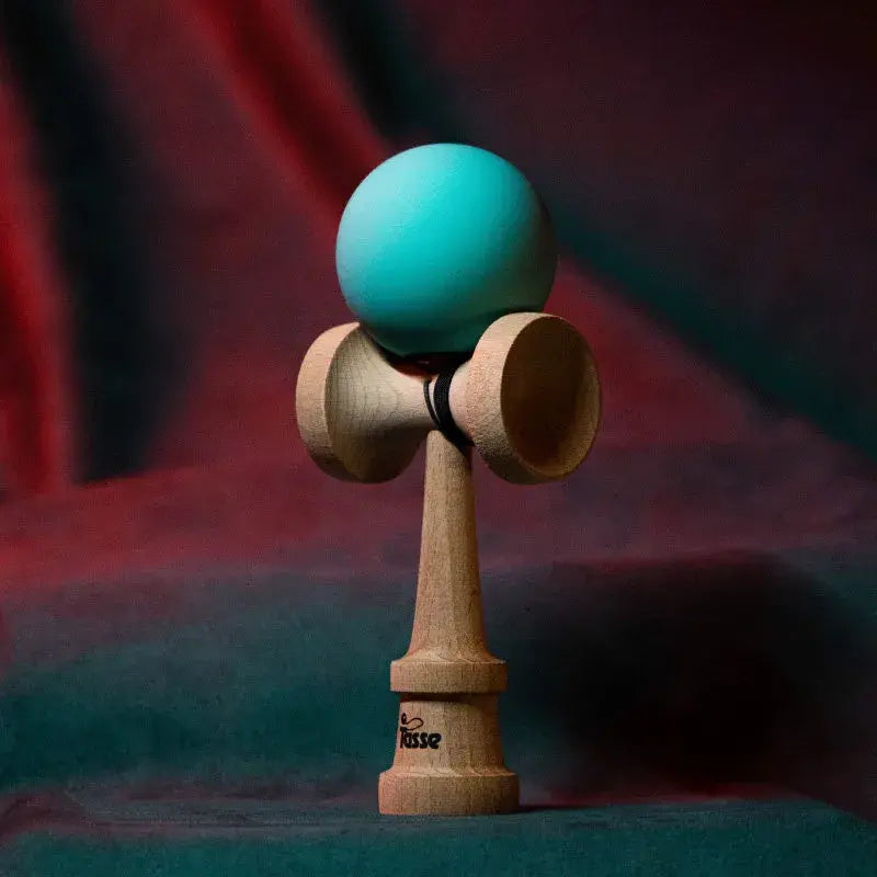 Tasse wooden kendama with a matte teal ball and natural wood handle, displayed upright on a red and blue gradient background.