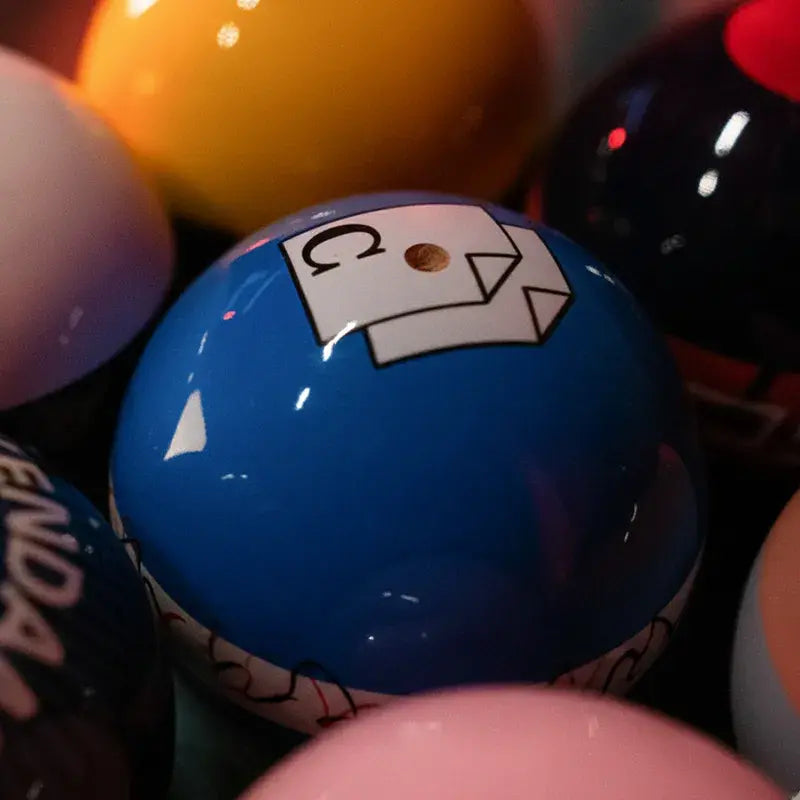 Close-up of a glossy blue Tasse kendama ball with white graphic detail, surrounded by colorful kendama balls in a dark background.