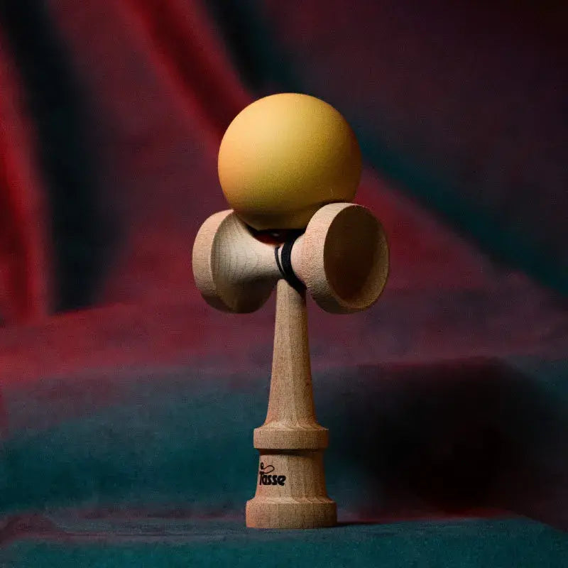 Tasse wooden kendama with a matte pale yellow ball and natural wood handle, displayed upright on a red and blue gradient background.