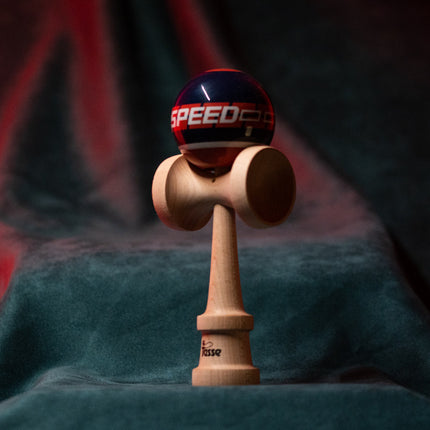 Tasse wooden kendama with a glossy navy ball, “SPEED” graphic detail, and natural wood handle, displayed upright on a red and blue background.