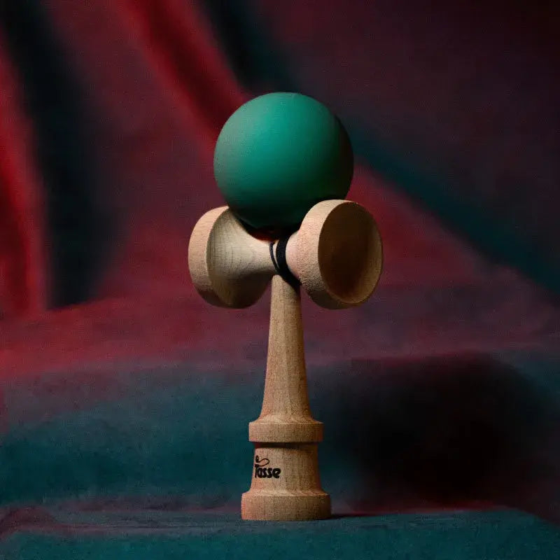Tasse wooden kendama with a matte deep teal ball and natural wood handle, displayed upright on a red and blue gradient background.