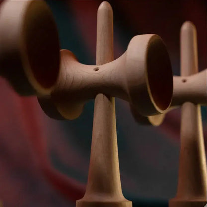 Close-up of a Tasse wooden kendama handle and cup details, with another kendama blurred in the background against a red and blue backdrop.